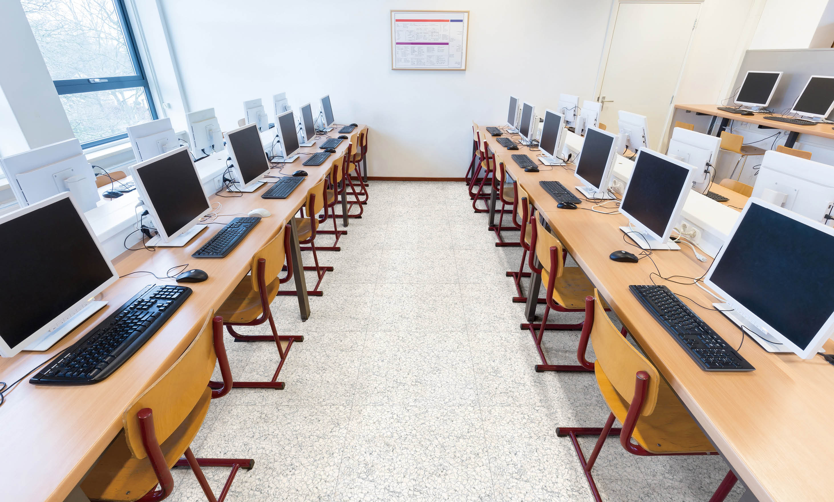 Desktop computers in computer lab on high school. On high school the students learn to use computers. The teenagers can sit in this classroom as a group but usually they work individually so they can get practical exercise with these electic devices. The teacher can see what everyone is doing in this computer network.